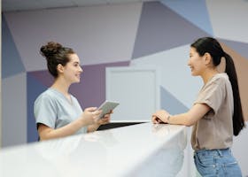 A receptionist and a visitor engaging at a modern reception desk, indoors.